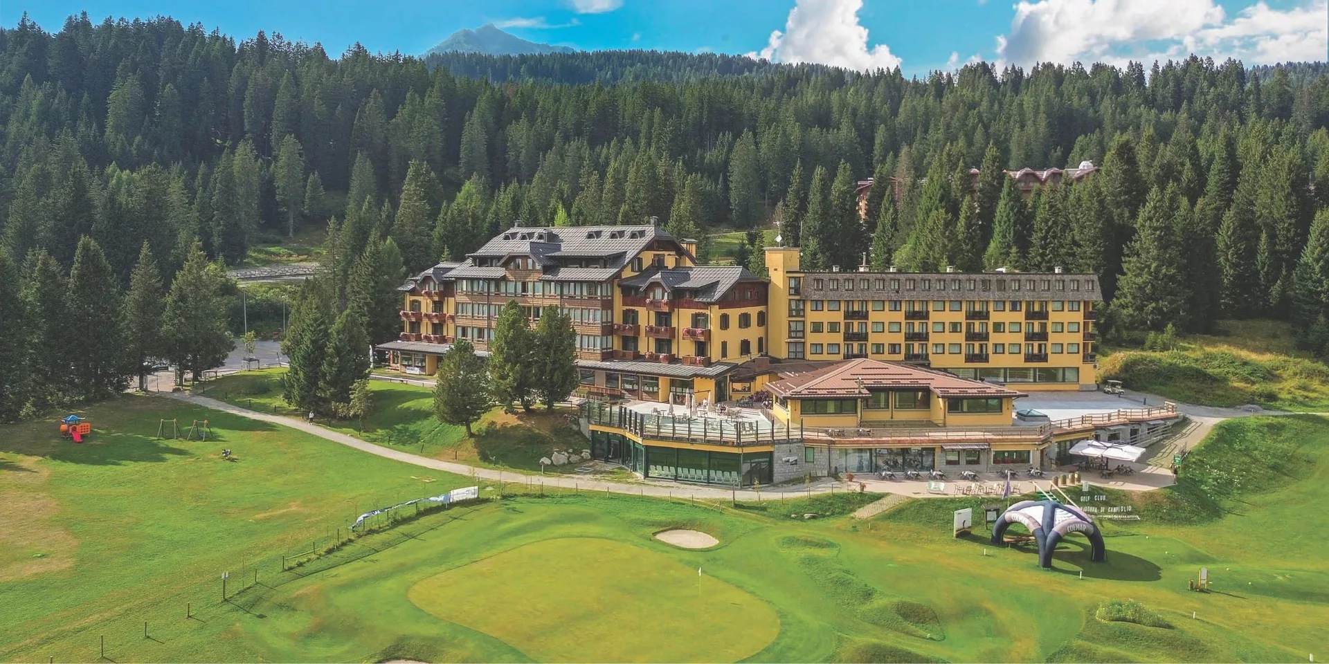 Vista aerea estiva dell'hotel di montagna immerso nel verde con campo da golf