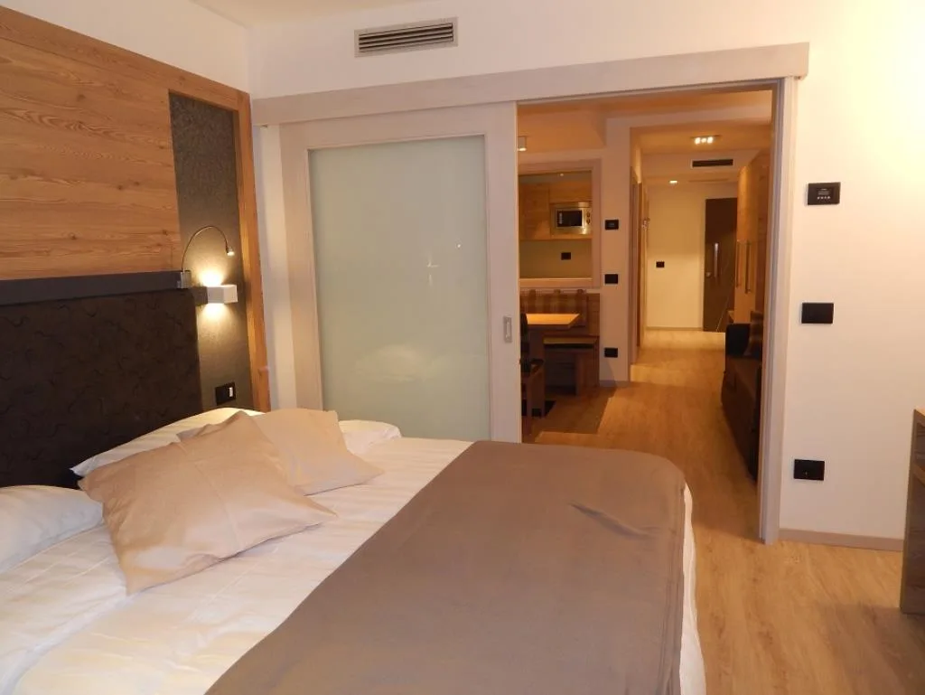 Camera moderna con testata in legno, letto matrimoniale e zona living con angolo cottura