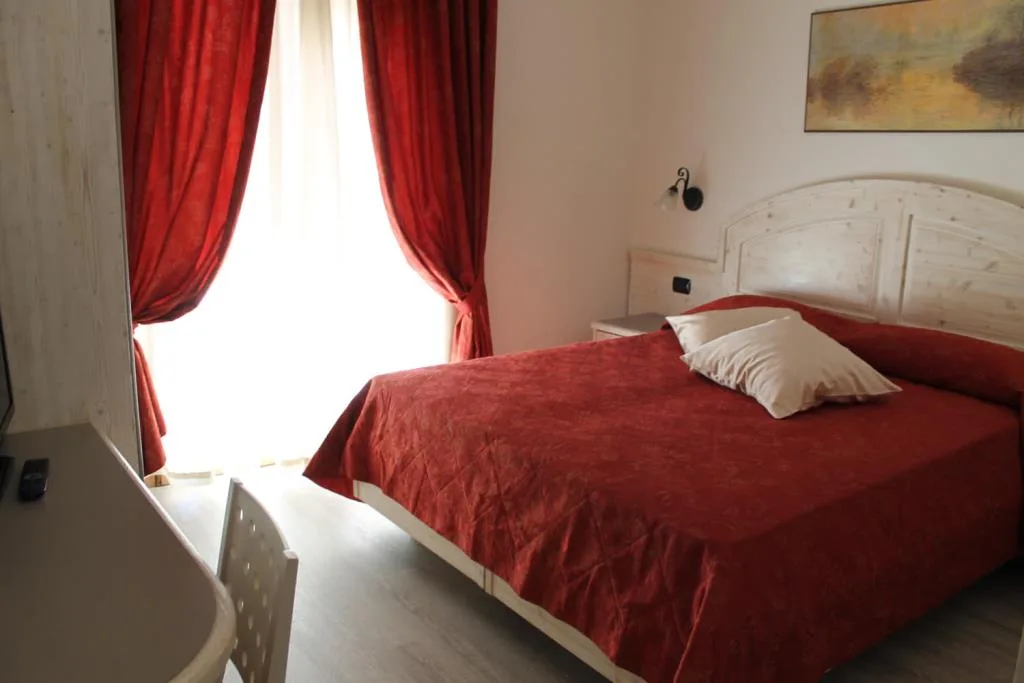 Camera con letto matrimoniale, copriletto rosso e tende rosse alla finestra