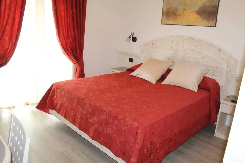 Camera matrimoniale con testata bianca, copriletto rosso e tende rosse
