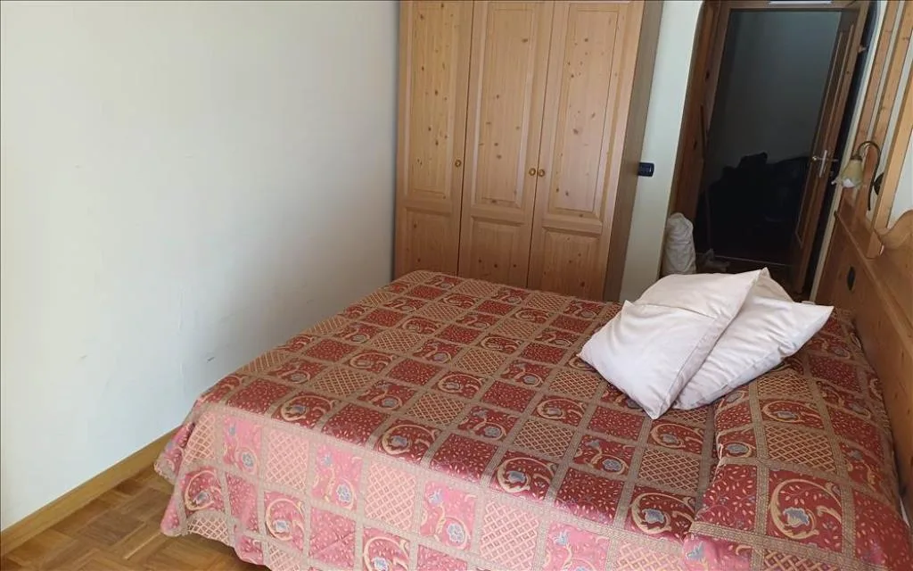 Camera semplice con letto matrimoniale, armadio in legno e copriletto a fantasia