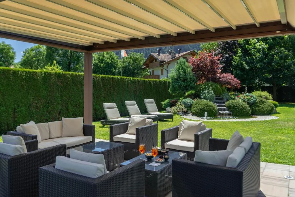 Area lounge esterna con divani in rattan sotto pergolato affacciata sul giardino