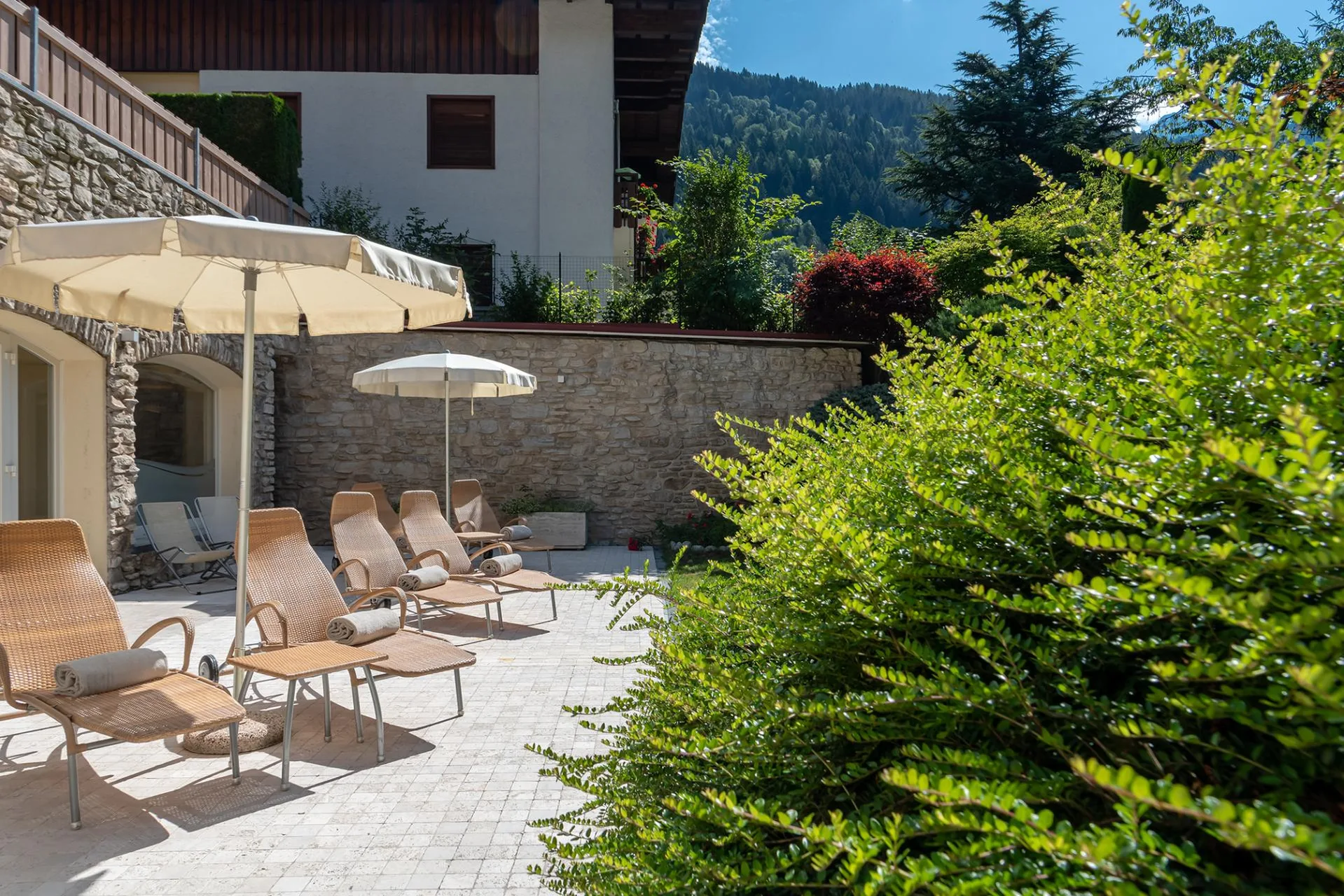 Terrazza esterna con lettini in vimini e ombrelloni accanto al verde