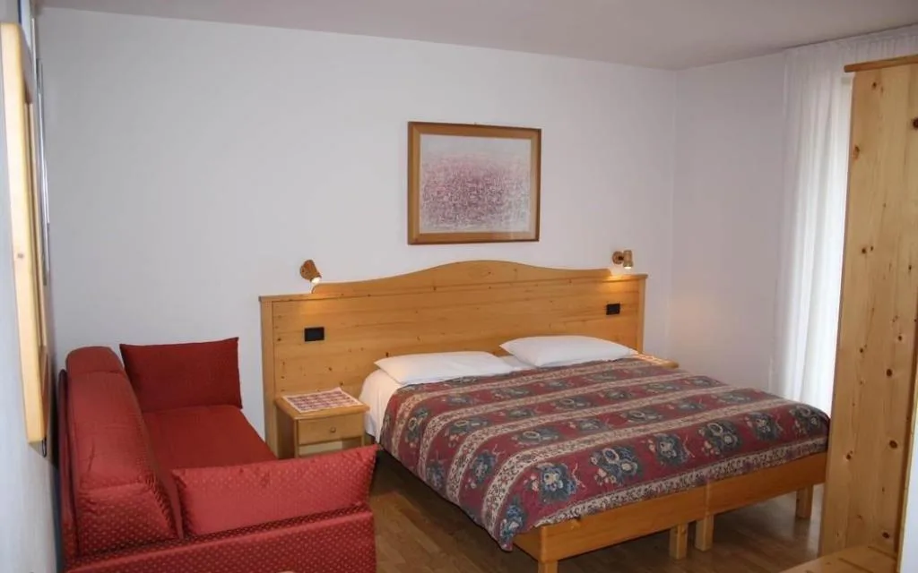 Camera con letto matrimoniale in legno e divanetto rosso