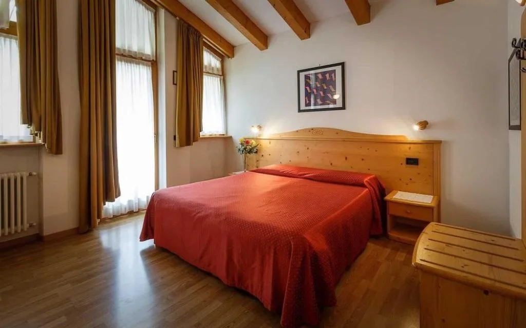 Camera matrimoniale con letto dal copriletto rosso, arredi in legno e ampie finestre
