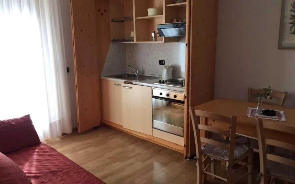 Angolo cottura di un monolocale con divano letto e tavolo in legno