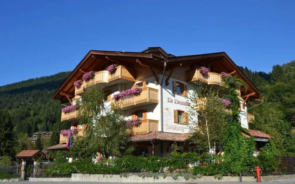 Facciata dell'Hotel La Locanda con balconi fioriti sotto un cielo azzurro estivo