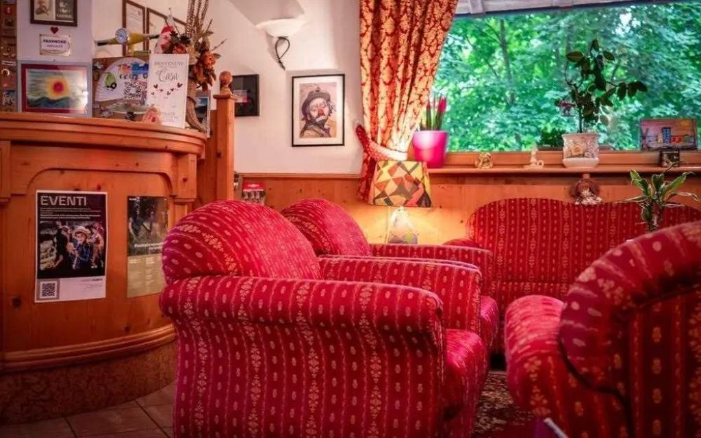 Zona lounge con poltrone rosse, reception e finestra affacciata sul verde