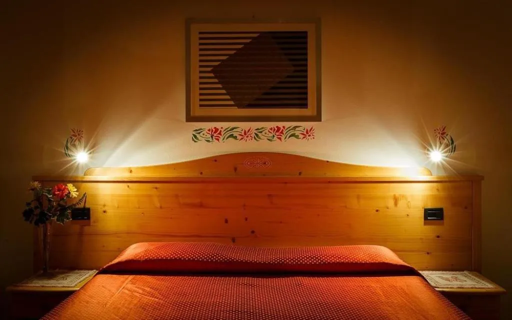 Dettaglio di letto matrimoniale con testiera in legno, luci e decorazioni floreali